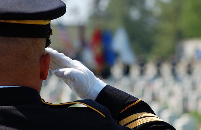 Man in military uniform salutes in front of graves in a cemetery.