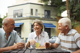 Senior couple and mature man having drinks at outdoor cafe, smiling