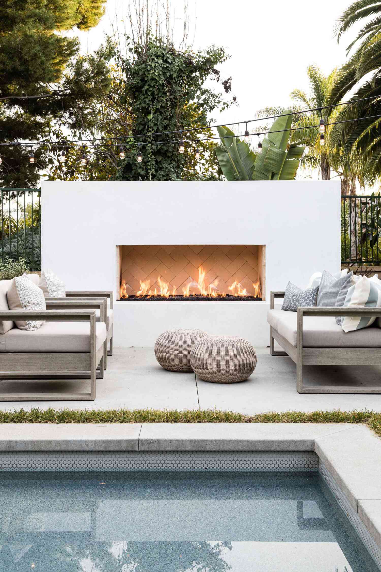 A backyard patio with cozy seating, a pool, an outdoor fireplace, and string lights