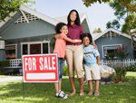 Mom and two kids standing beside "for sale" sign in front of home