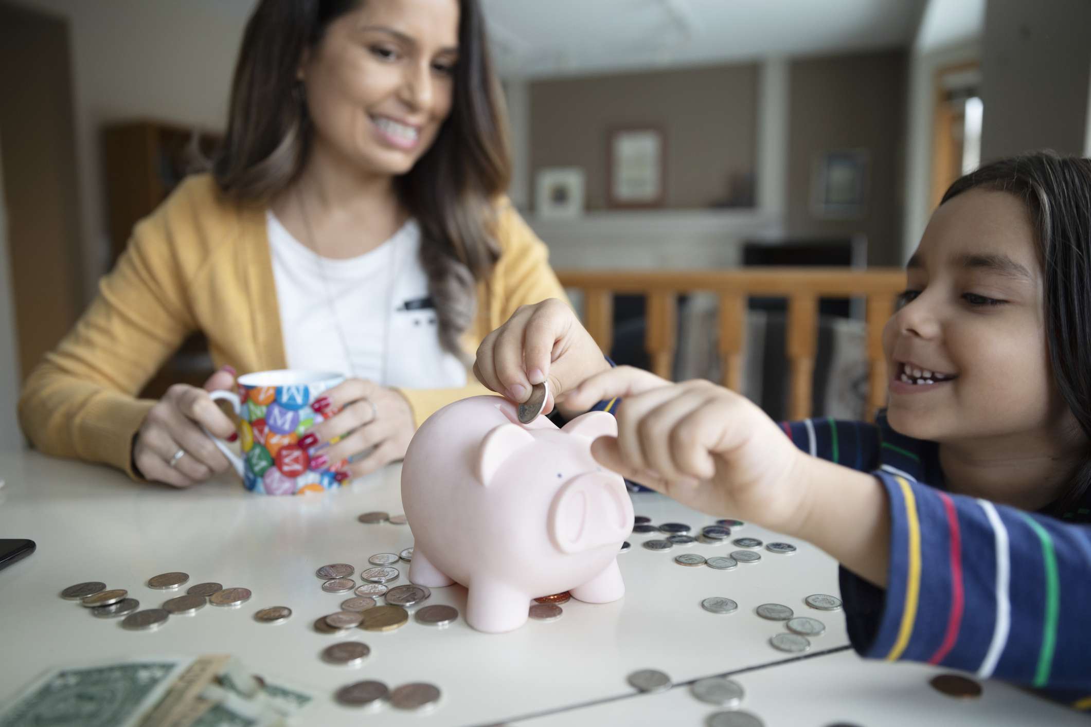 Mother watching son place coins in piggy bank.