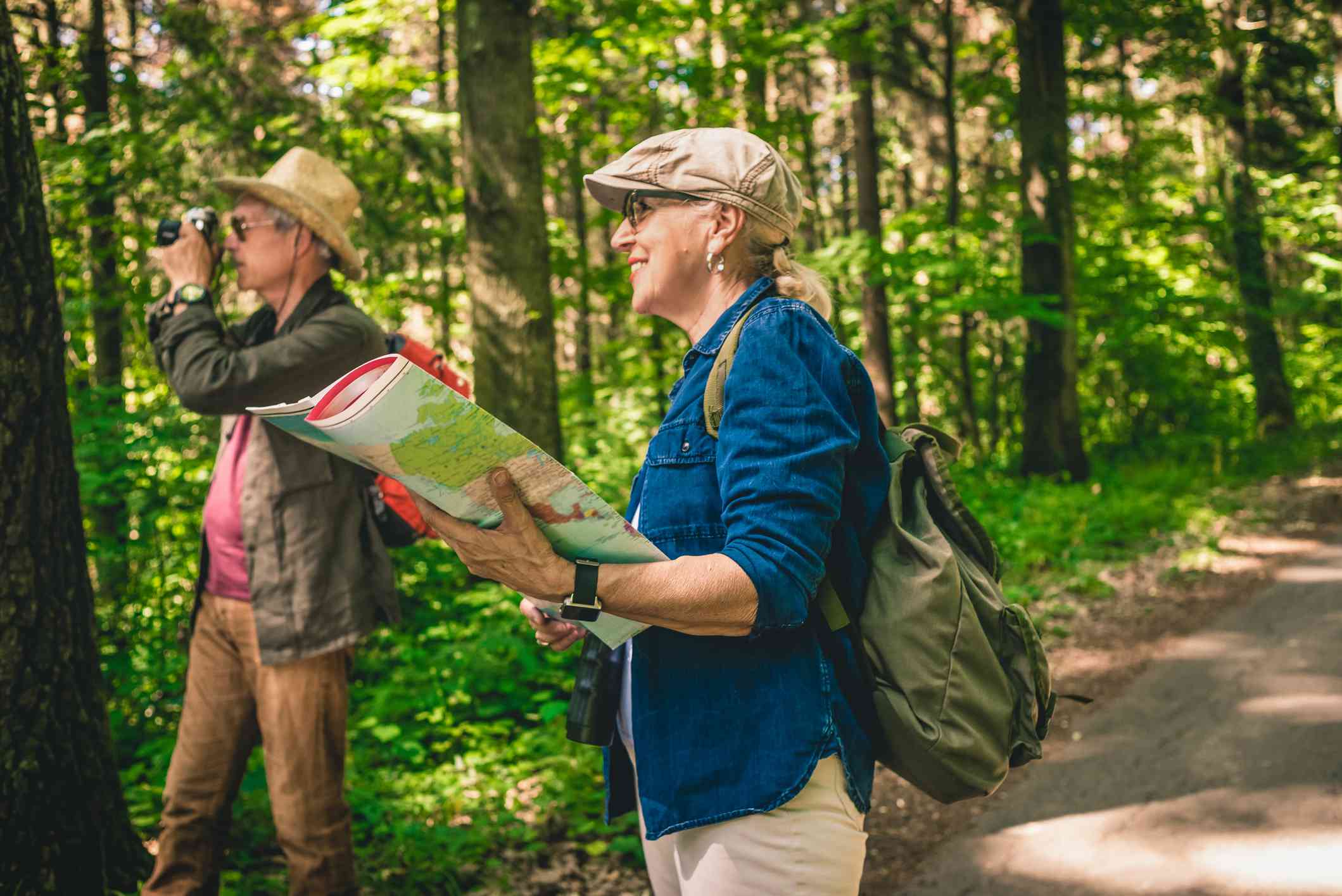 older senior couple uses field guide books to identify trees in forest