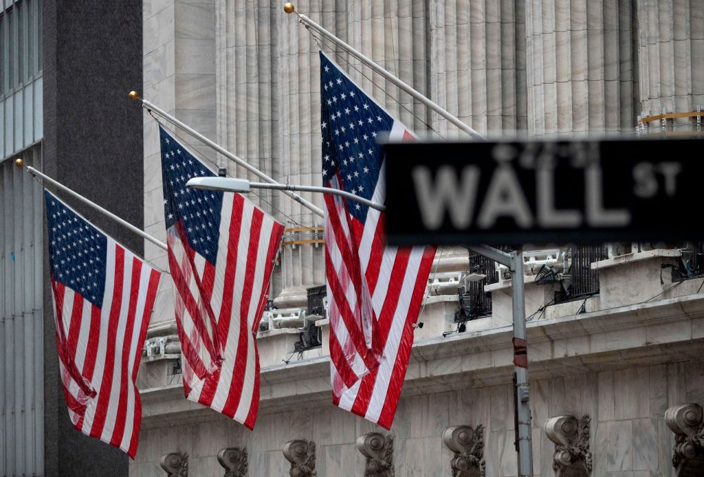 The "Wall St" street sign is seen near US flags in front of the New York Stock Exchange (NYSE) on a rainy day on Wall Street in New York City