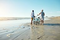 Elderly couple walking with bikes on the beach