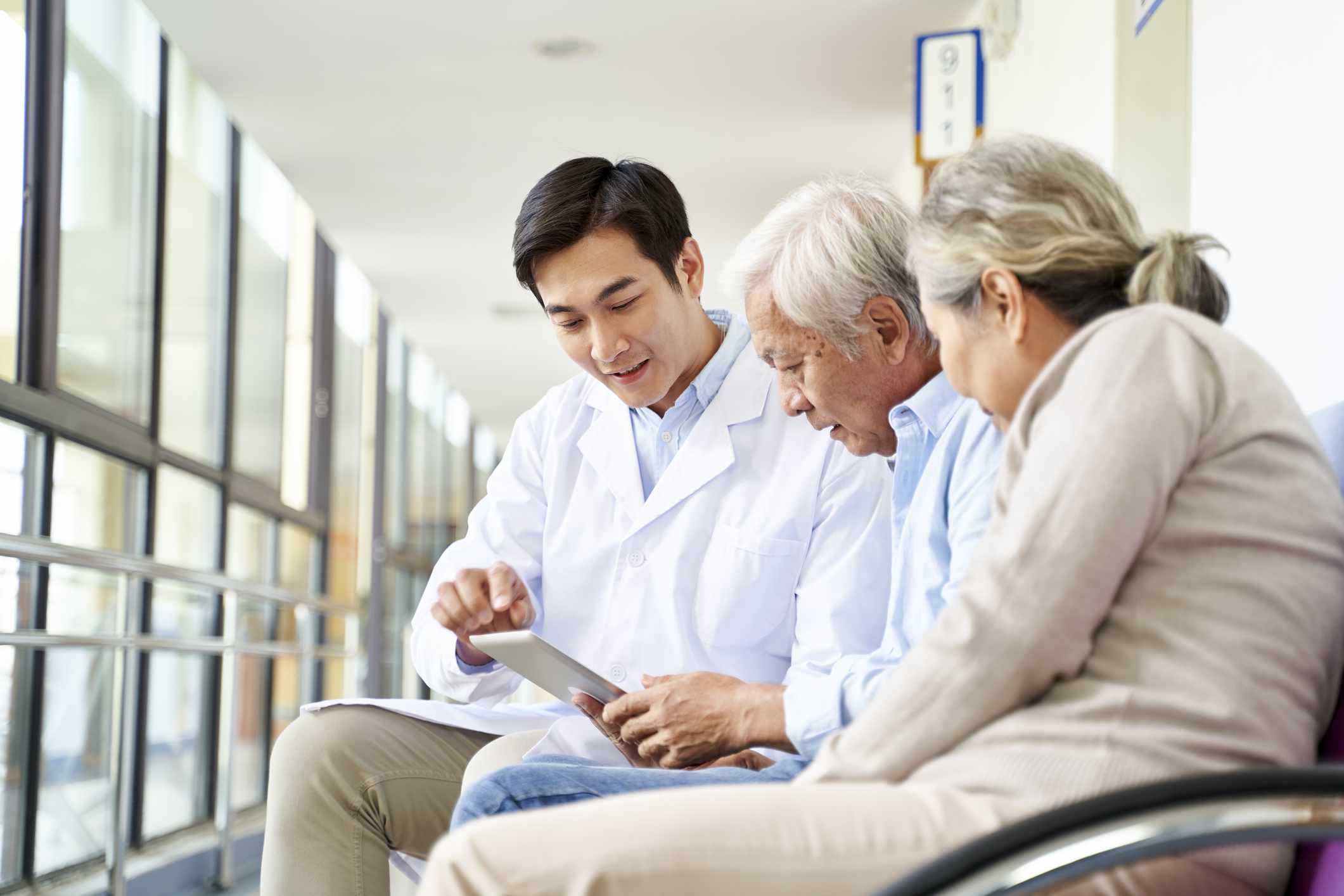 Elderly couple speaking with a doctor in a hospital looking at a tablet