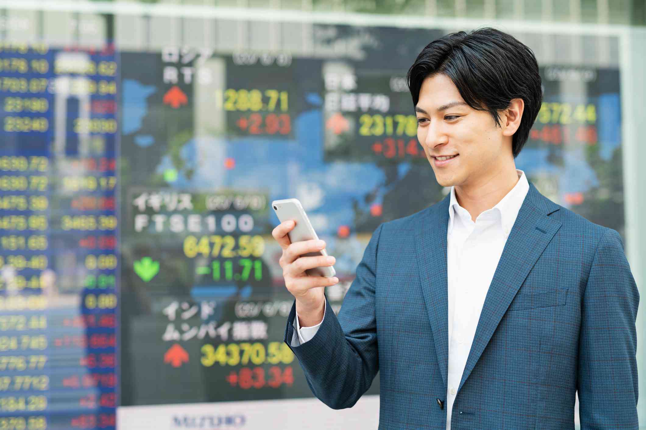 Asian man holding phone in front of stock ticker data
