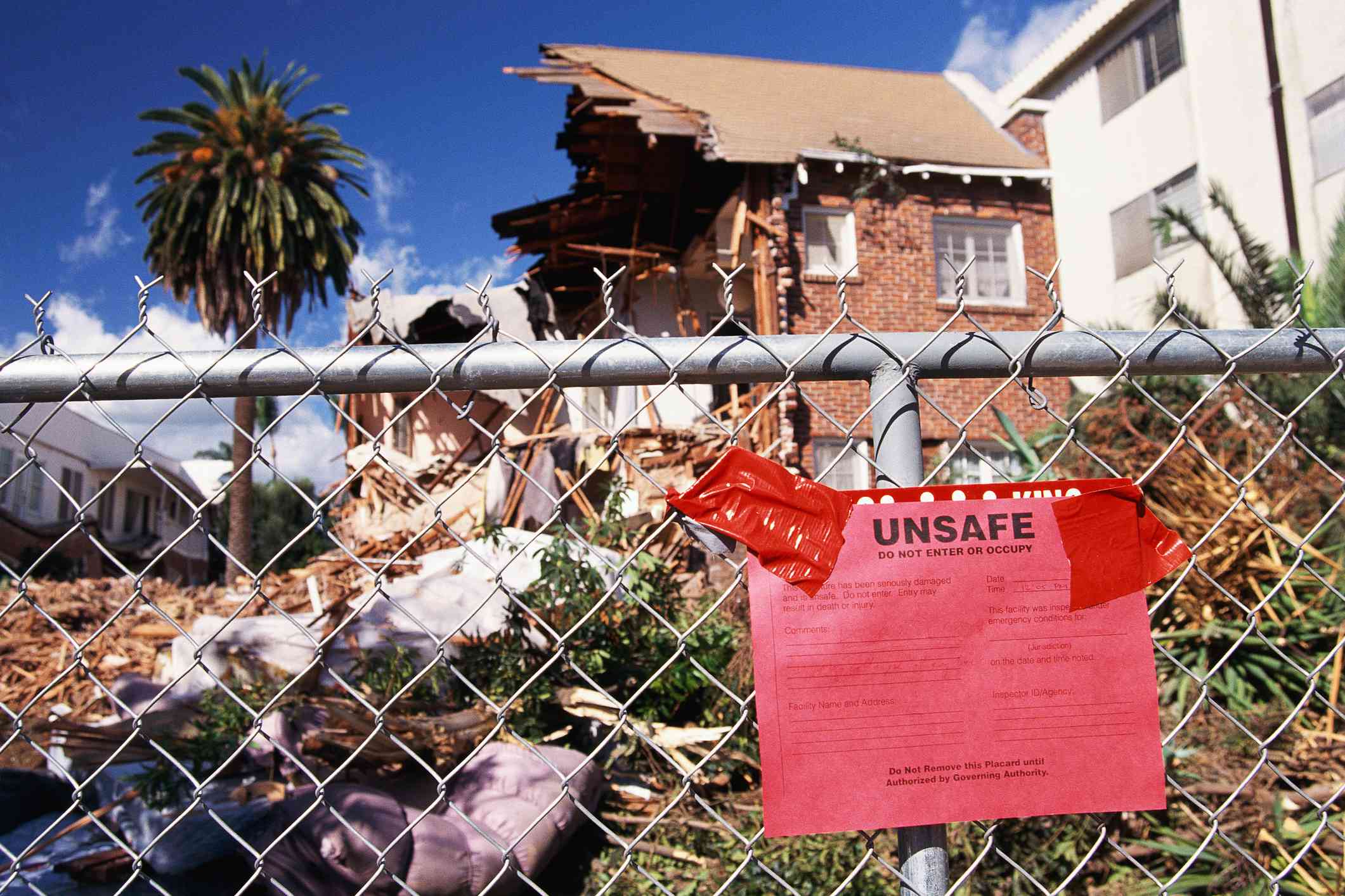 Home destroyed by hurricane, with “Unsafe” sign taped to chain-link fence