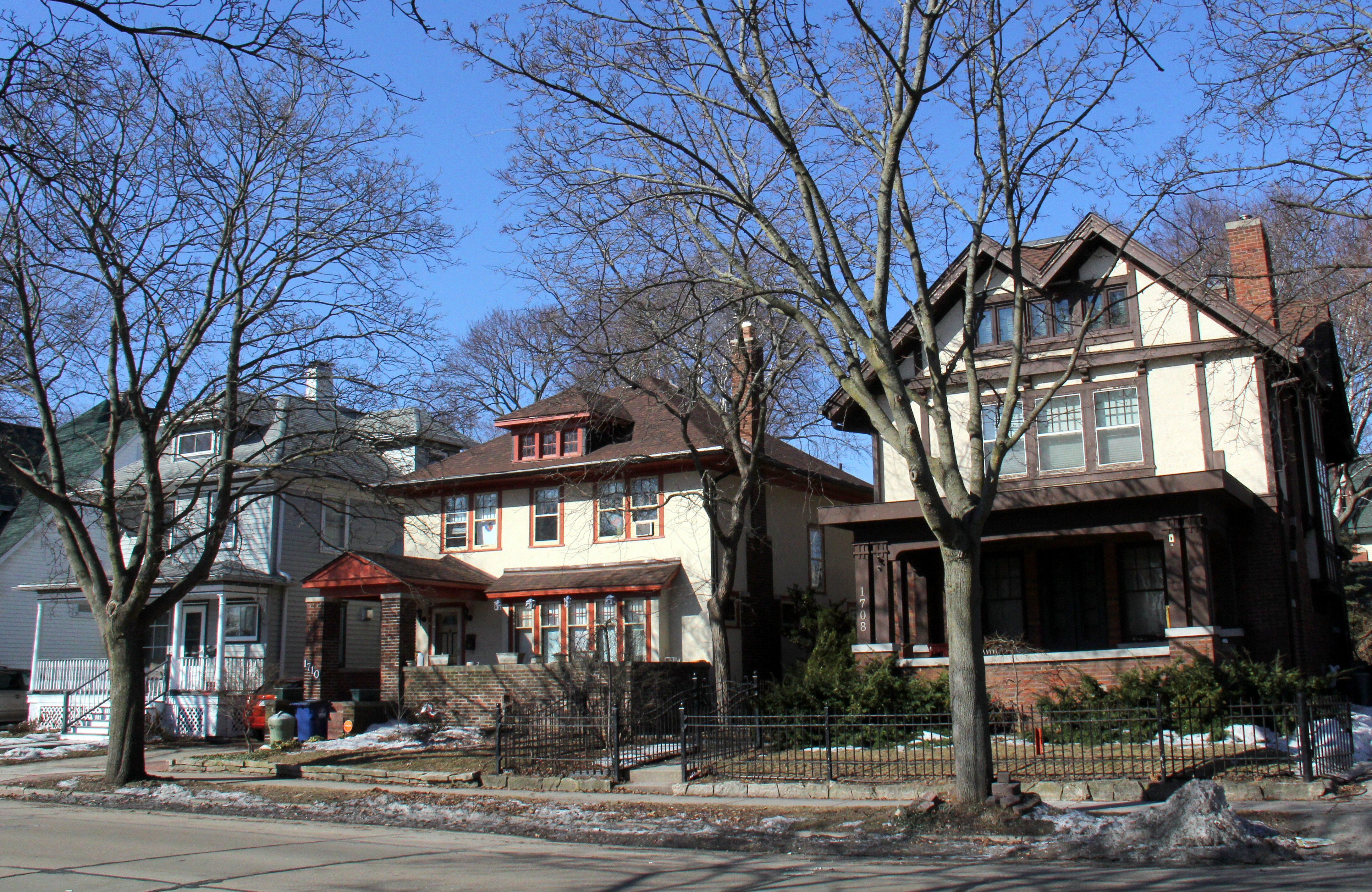 Suburban American street with three houses of various revival stylings close together and close to the sidewalk