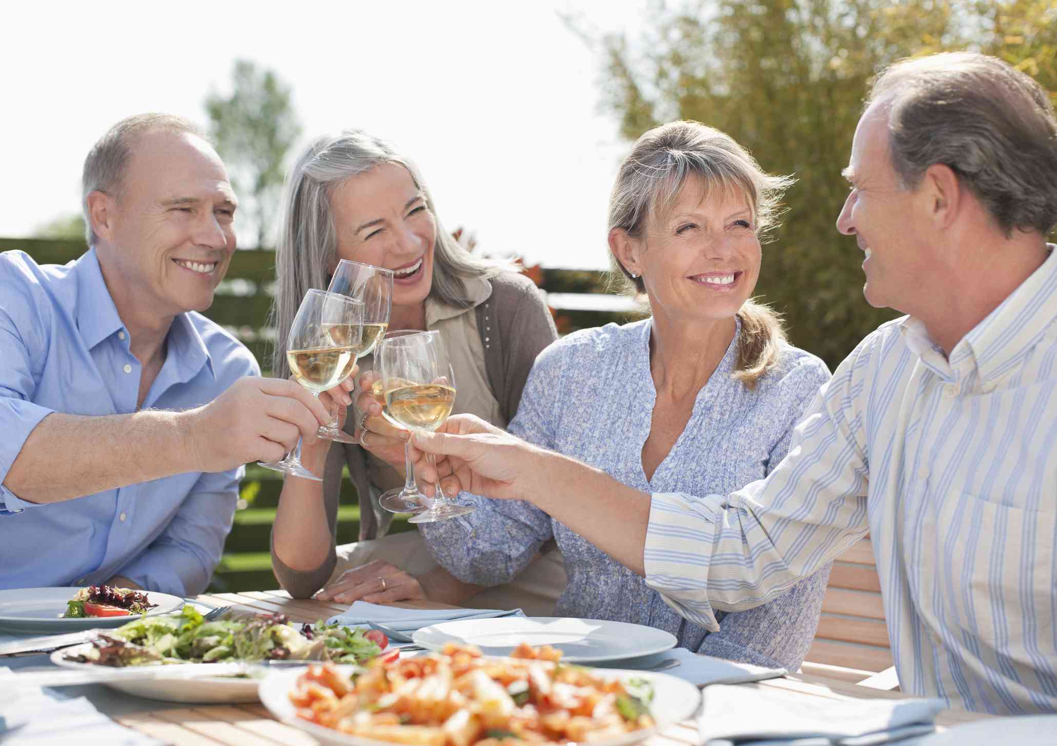 Two senior couples toast with glasses of wine.