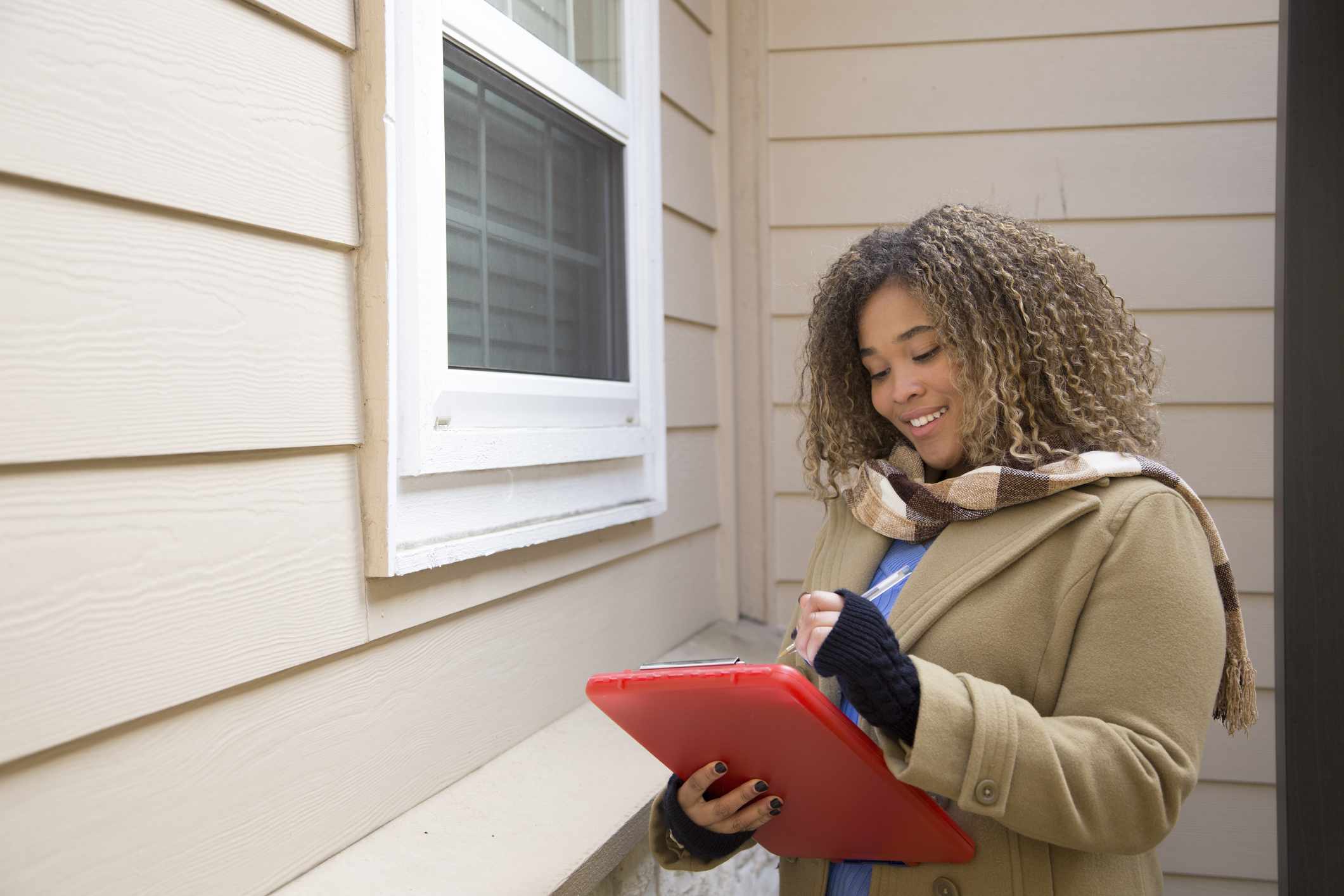 Woman in winter clothes outside home makes notes on clipboard