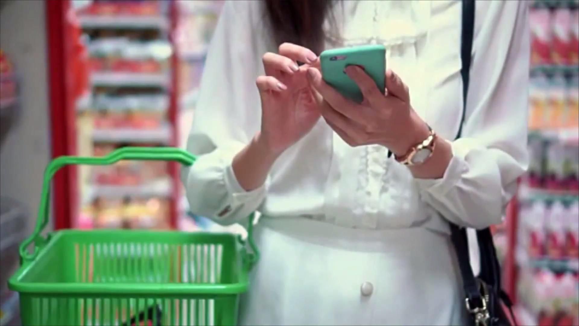 Woman Holding Phone Calculator with Market Basket at Store